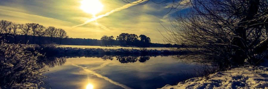 Winterlandschaft mit Fluss, Wiese, Sonne, blauem Himmel und Kondenzstreifen