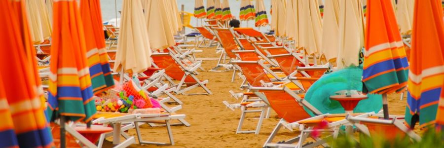 Der Strand von Bibione mit vielen Liegen und orangenen Sonnenschirmen.