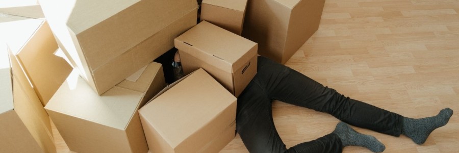 Eine Person in schwarzer Hose liegt unter einem Haufen Pappkartons.
